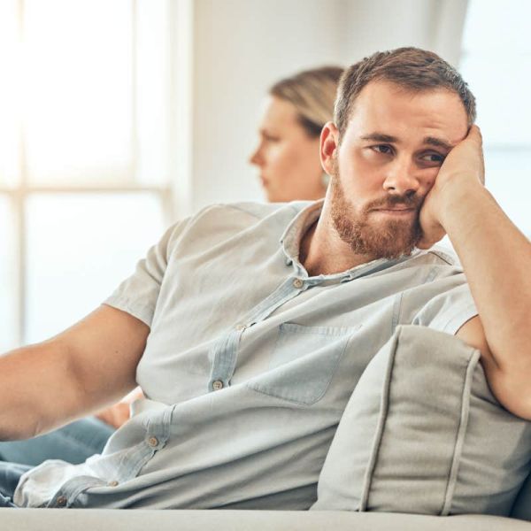 Young caucasian man with a beard looking unhappy and annoyed while sitting on the couch during an argument with his wife at home