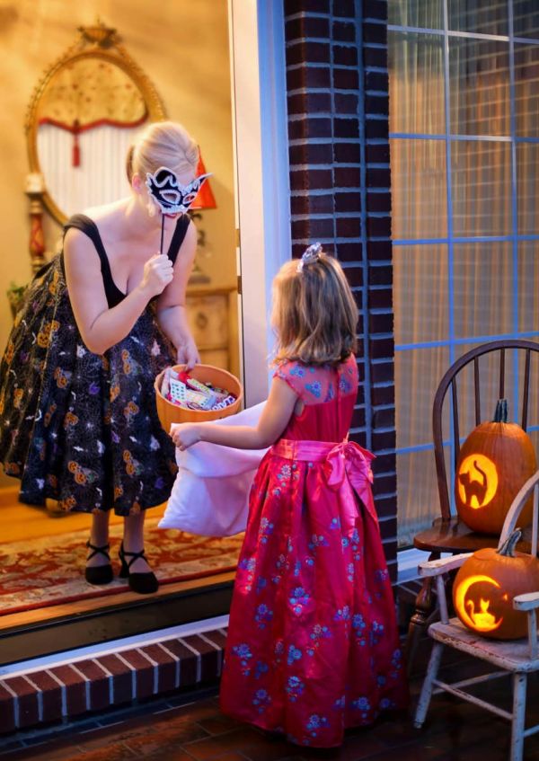 woman handing out candy at her door to little girl on halloween