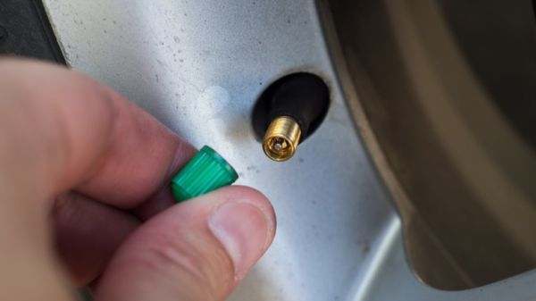 A person removing a green nitrogen valve stem cap