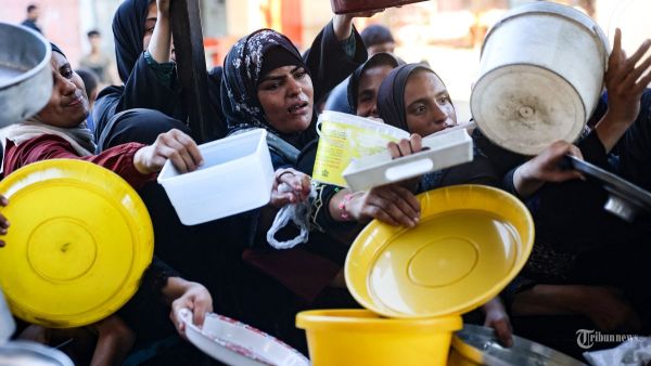 Para wanita Palestina mengulurkan piring mereka ke arah seorang pria, untuk menerima jatah roti sayur yang disiapkan oleh para sukarelawan di Beit Lahia di Jalur Gaza utara pada tanggal 14 Agustus 2024, di tengah konflik yang sedang berlangsung antara Israel dan kelompok militan Hamas. (Photo by Omar AL-QATTAA / AFP)