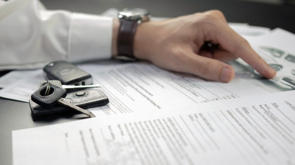 A person looking over car- documents, with keys on the table.