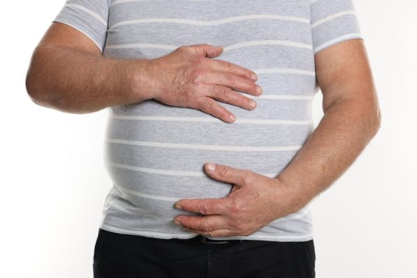 Closeup of an overweight man in a tight t-shirt holding his stomach, isolated on white background