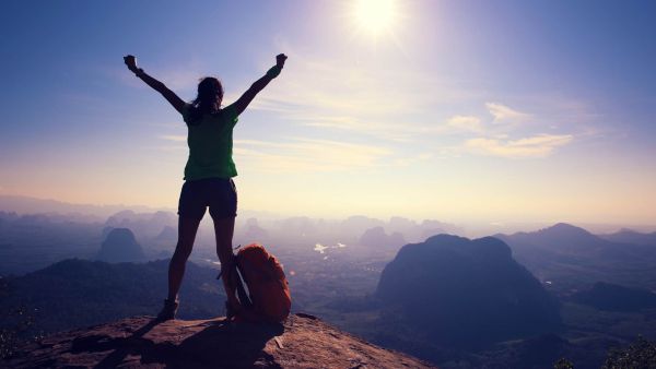 woman with arms raised at the top of a mountain