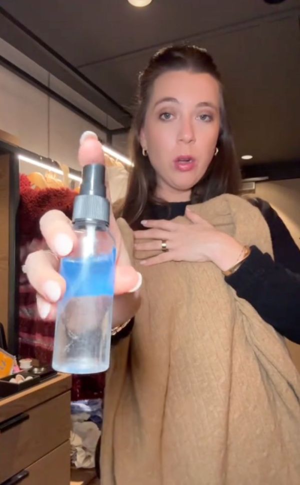 A woman holding a spray bottle demonstrating a fashion hack for removing odor from clothes using vodka