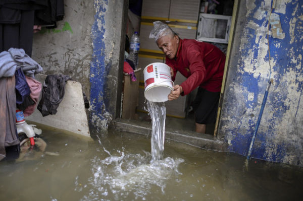 Seorang warga berusaha membuang air yang meluap ke dalam rumahnya di kawasan Grogol, Jakarta Barat, saat dilanda banjir pada 29 Januari 2025. Foto: Jamal Ramadhan/kumparan