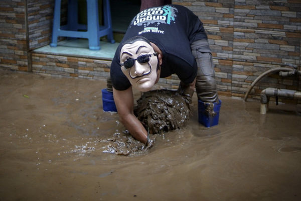 Warga yang memakai topeng membersihkan lumpur yang terbawa banjir di kawasan Kampung Melayu pada 16 Juli 2022. Foto: Jamal Ramadhan/kumparan