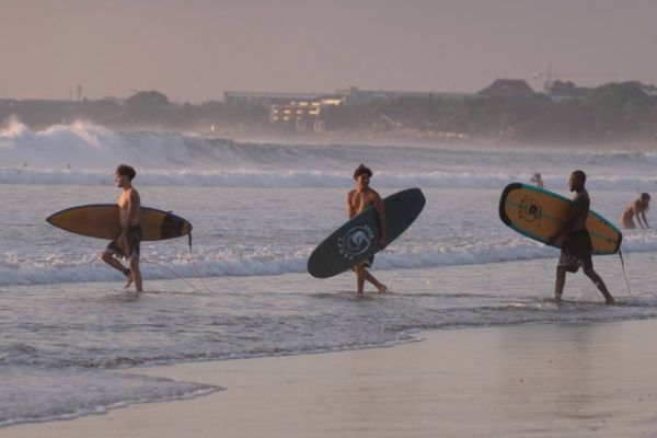 Sejumlah wisatawan membawa papan selancar berjalan menuju ke tengah laut saat berlibur di Pantai Kuta, Badung, Bali. Foto: Nyoman Hendra Wibowo/Antara Foto