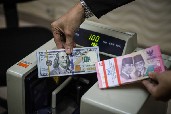 Seorang petugas menunjukan pecahan Dolar AS dan Rupiah di salah satu tempat penukaran mata uang asing di Kwitang, Jakarta, Senin (9/12/2024). Foto: Iqbal Firdaus/kumparan