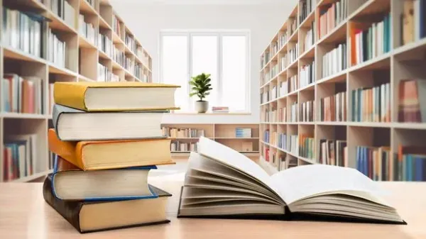 Book stack and opened book on the desk on blurred bookshelves in light public library room background