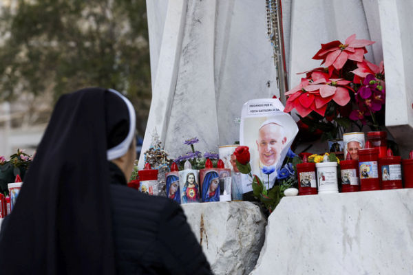 Seorang biarawati berdoa saat lilin dan bunga diletakkan di dasar patung mendiang Paus Yohanes Paulus II di luar Rumah Sakit Gemelli tempat Paus Fransiskus dirawat, di Roma, Italia, Minggu (23/2/2025). Foto: Ciro De Luca/REUTERS