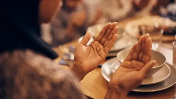 Close-up of religious Muslim woman and her family praying before the meal at dining table on Ramadan.