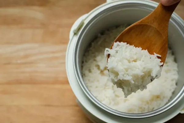 Jasmine rice cooking in electric rice cooker with steam, Hand hold wooden ladle in electric rice cooker in the kitchen.