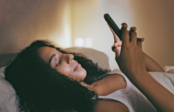 woman on phone in bed with happy face, texting in house. 