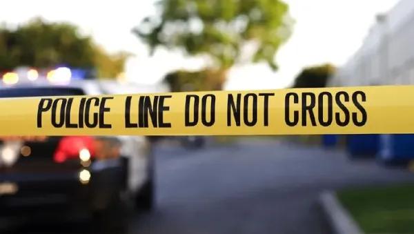 A blurred police car in the background behind yellow crime scene tape.