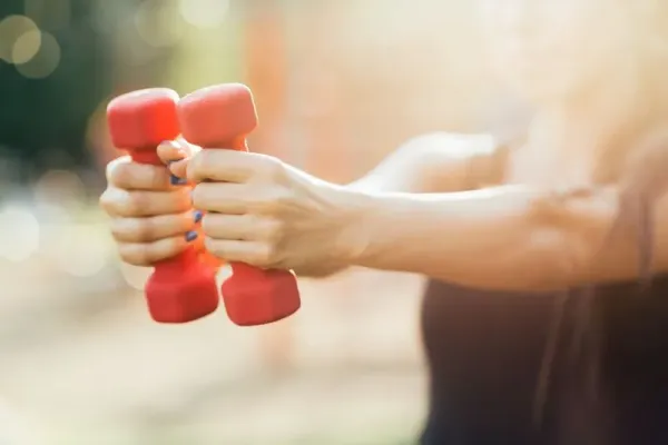 Girl making exercises with dumb-bells in the park. Shalow depth of field.