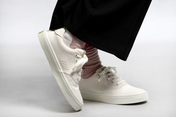 A person in a pair of white canvas sneakers, baggy socks and black pants.