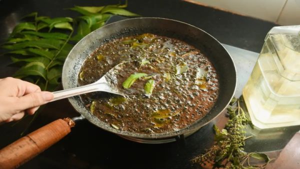 A PAN of Simmering Oil With Amla, Methi, and Green Leaves Being Stirred on a Stovetop to Make Herbal Hair Oil.