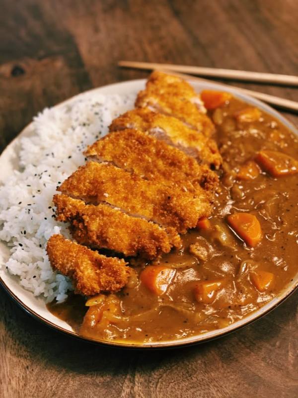 This may contain: a white plate topped with meat and rice next to chopsticks on a wooden table