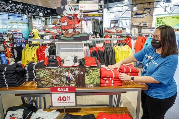 A retail worker wearing a face mask adjusts a display of Columbia sportswear at a Walt Disney World store.
