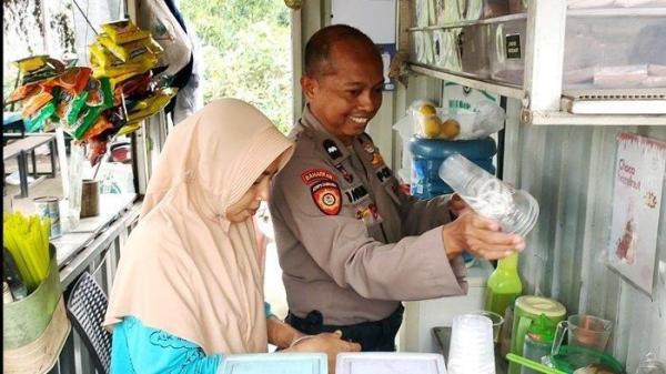 KEDAI ES POLISI: Kasubnit I Dalmas Polres Bangkalan, Aipda Khoirul Anam memanfaatkan waktu istirahat berdinas dengan menyambangi Kedai Babin Ice yang dijaga isterinya, Eka Widiyati di depan Pasar/Kecamatan Socah, Senin (30/6/2025).