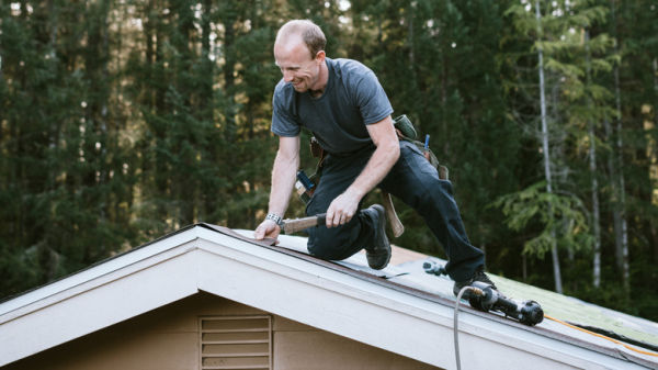 Man fixing shingles on the roof of a house