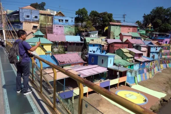 Wisatawan berjalan di jembatan kaca saat mengunjungi Kampung Warna-Warni Jodipan di Malang, Jawa Timur, Kamis (20/7/2023). Kampung warna-warni yang dibuka sebagai objek wisata sejak tahun 2016 tersebut saat ini dicat ulang secara bertahap pada ratusan rumah milik warga setempat yang dimulai dari awal tahun 2023 untuk meningkatkan jumlah kunjungan wisata. ANTARA FOTO/Nyoman Hendra Wibowo/rwa.