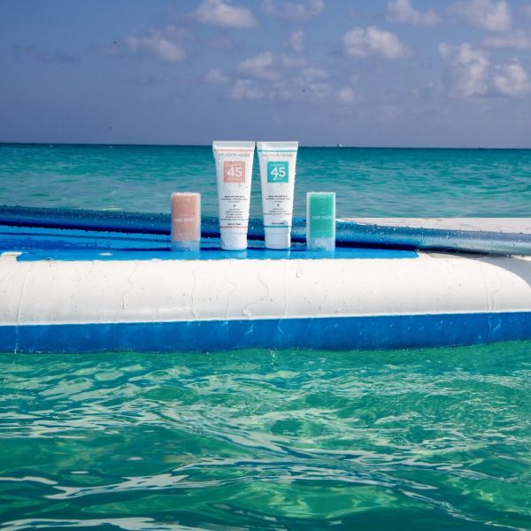 Three bottles of sunscreen and two tubes of sunscreen paste on a paddleboard in the ocean.