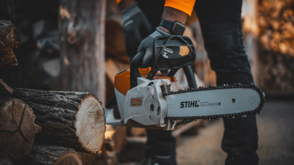 Gloved hands holding a cordless STIHL chainsaw