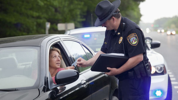 A woman in a black car handing her license to a police officer after being pulled over