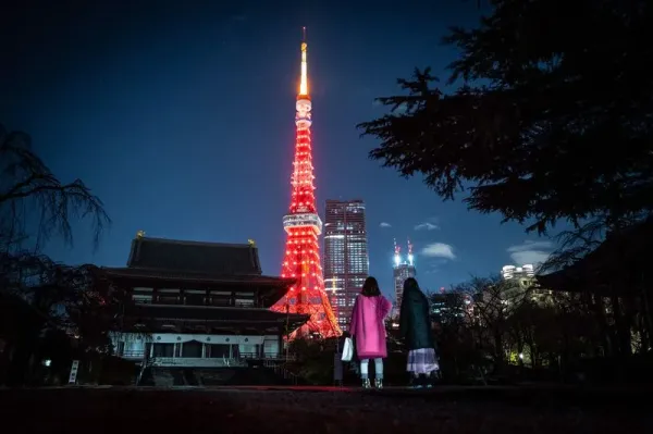 People wait to cross a street as Tokyo Tower is lit in red to celebrate the Chinese Lunar New Year in Tokyo on January 21, 2023. (Photo by Yuichi YAMAZAKI / AFP) (Photo by YUICHI YAMAZAKI/AFP via Getty Images)