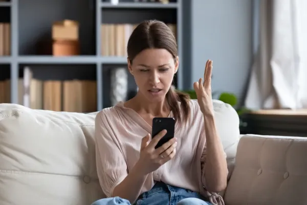 Young woman looking frustrated while using her phone on a couch.