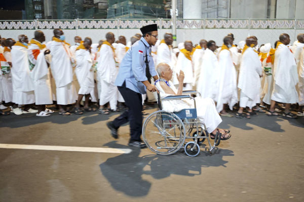 Petugas layanan lansia PPIH Arab Saudi Abdurrahman mendorong kursi roda yang dinaiki calon haji lansia Soemarno menuju Masjidil Haram untuk menunaikan umrah wajib. Foto: Andika Wahyu/ANTARA FOTO