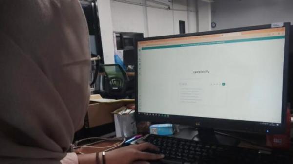GUNAKAN AI - Adhila Paramitha Larasati, mahasiswa jurusan Manajemen Administrasi Universitas Sebelas Maret Surakarta (UNS) saat menggunakan sebuah platform AI pada komputer yang digunakannya, Kamis (27/11/2025).
