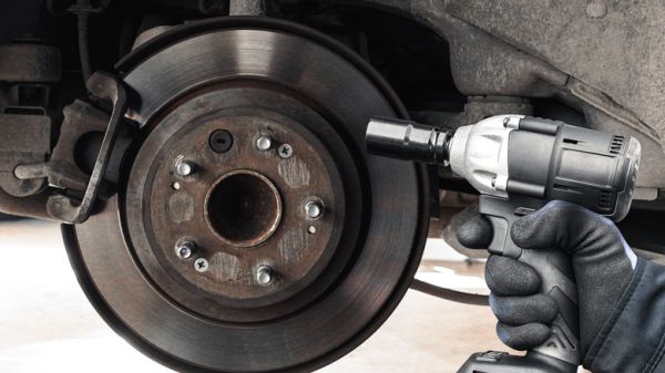 Cordless impact wrench being held next to brake caliper and rotor