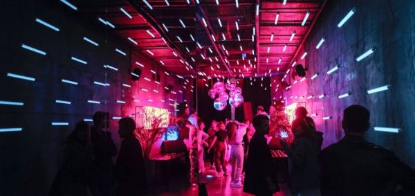 This may contain: a group of people standing in a tunnel with neon lights on the walls and floor