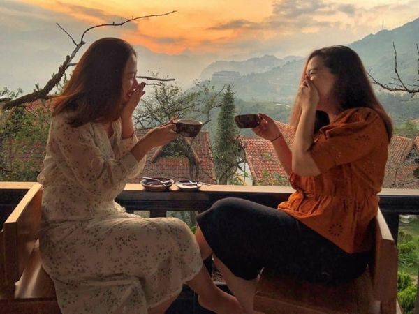 This may contain: two women sitting at a table drinking coffee and looking out over the mountains in the distance