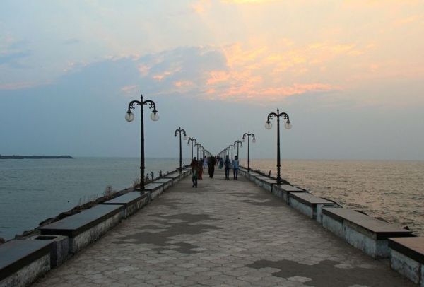 This may contain: people walking on a pier near the ocean at sunset or dawn with clouds in the sky