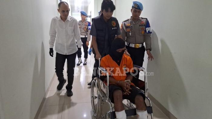 DIKAWAL KETAT -- Pelaku Ad (27) dengan dikawal ketat anggota, saat keluar dari ruang aula SAR dan menuju sel tahanan Mapolresta Pangkalpinang, Selasa (30/12/2025).