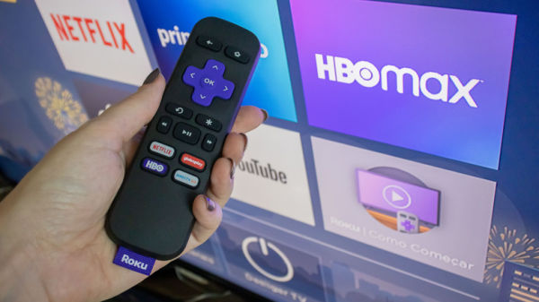 A person holding a Roku remote in front of a Roku TV