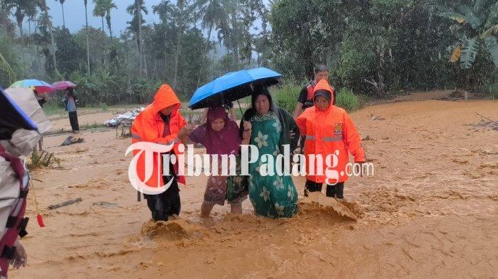 BANJIR DI PADANG- Petugas Basarnas membatu dua orang ibu-ibu melewati derasnya arus banjir yang menerjang permukiman warga di Pasar Lalang, Kecamatan Kuranji, Kota Padang, Sumatera Barat, Jumat (2/1/2026) sore.