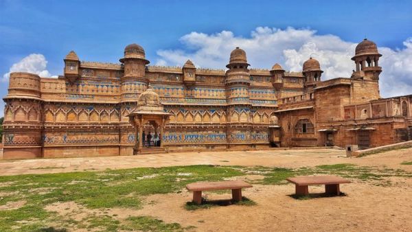 This may contain: a large building with two benches in front of it on a dirt field next to grass