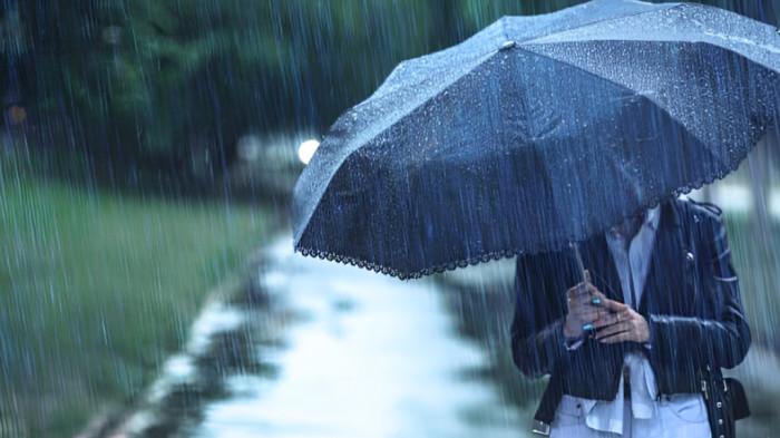 HUJAN LEBAT- Ilustrasi seorang wanita tengah menembus hujan lebat dengan membawa payung.