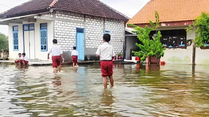 BANJIR LAMONGAN - Para siswa di SD Negeri 2 Desa Pasi tetap masuk sekolah meski dalam kondisi banjir akibat luapan Sungai Bengawan Jero yang kian meluas di Kabupaten Lamongan, Jawa Timur, Selasa (13/1/2026).
