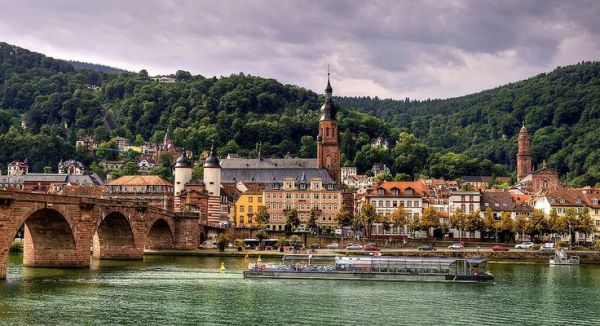This may contain: an old bridge over a river with boats in the water and mountains in the background