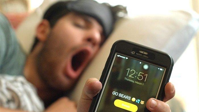 Ilustrasi pria bangun tidur karena alarm ponsel.