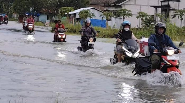 TERJANG BANJIR - Sejumlah pengendara sepeda motor nekat menerjang banjir di Jalan Raya Pati-Gabus, Sabtu (17/1/2026).