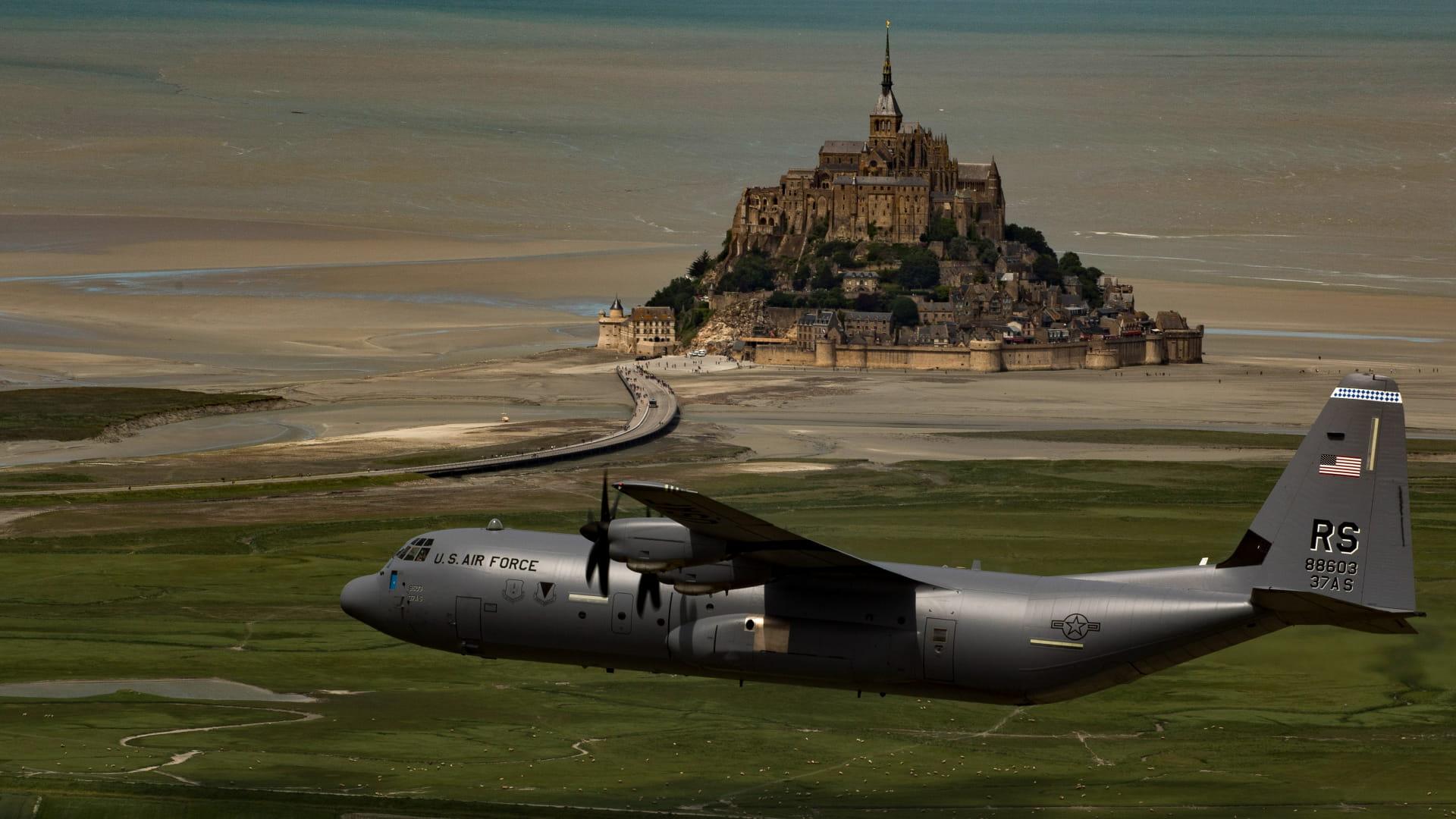 PANGKALAN UDARA AS - Foto yang diunggah di laman resmi Ramstein Air Base, memperlihatkan pesawat militer U.S. Air Force C-130 Hercules yang sedang terbang rendah di atas lanskap hijau dengan latar belakang Mont Saint-Michel, sebuah pulau bersejarah di Normandia, Prancis.