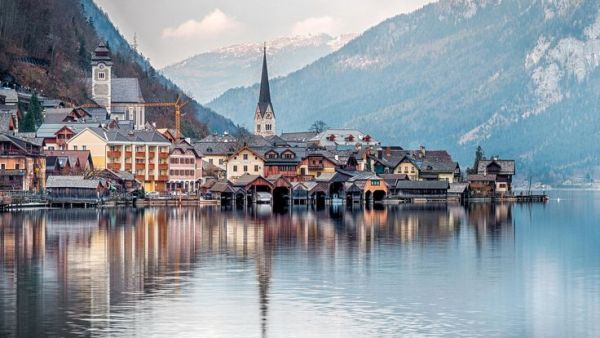 This may contain: a town on the shore of a lake with mountains in the background