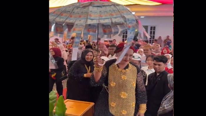 ROMPI EMAS - Umrah Sholehan, wanita asal Banjarmasin menjadi perbincangan setelah penampilannya mengenakan rompi emas dan payung uang beredar di media sosial. Pemilik toko emas menyebut rompi emas yang dipakai Umrah bernilai Rp9 miliar, Rabu (21/1/2026).
