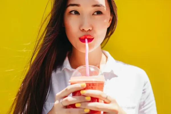 Asian woman drinking juice in a disposable plastic glass using a straw. Portrait of a young woman enjoying a glass of juice.